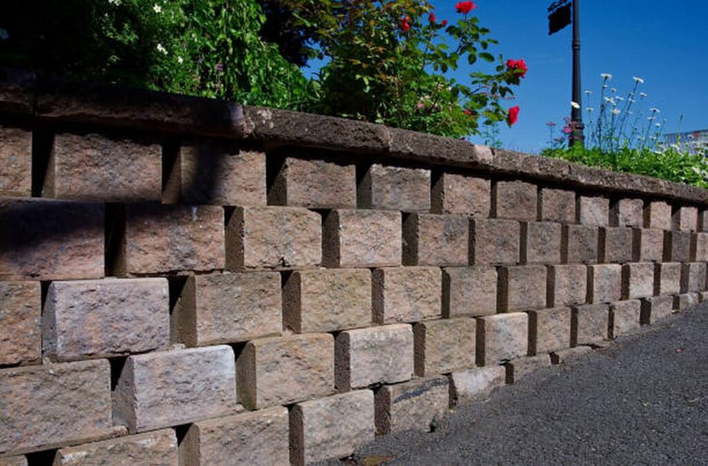 a side view of a concrete block retaining wall with planted flowerbed behind.